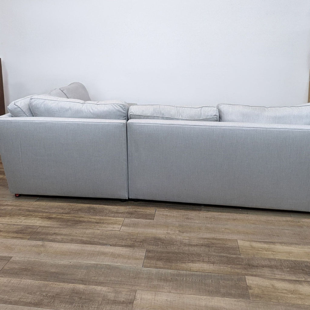 2. "Side view of a Pottery Barn ash-colored sectional couch with plush back cushions on a wooden floor."