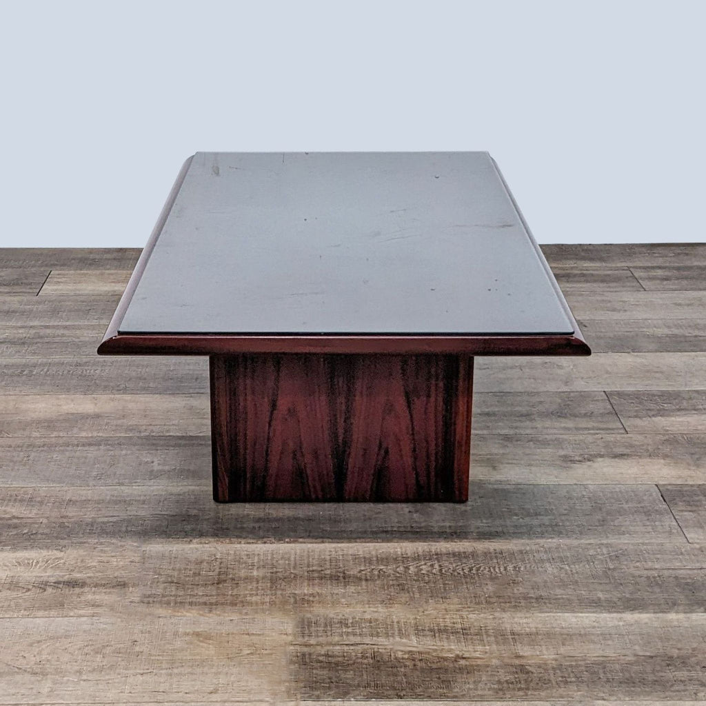 Front-facing image of Reperch glass-topped coffee table with wooden pedestal base on a wood floor.