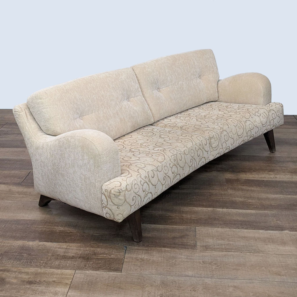 Two-seater Reperch couch featuring beige upholstery with scroll patterns and solid saddle arms on a wood floor.