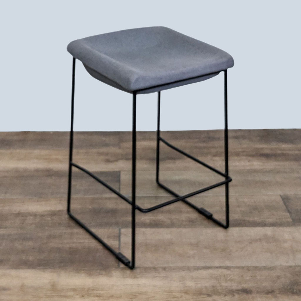 2. Sleek gray upholstered stool from EQ3 against a wood floor, featuring a geometric black base.