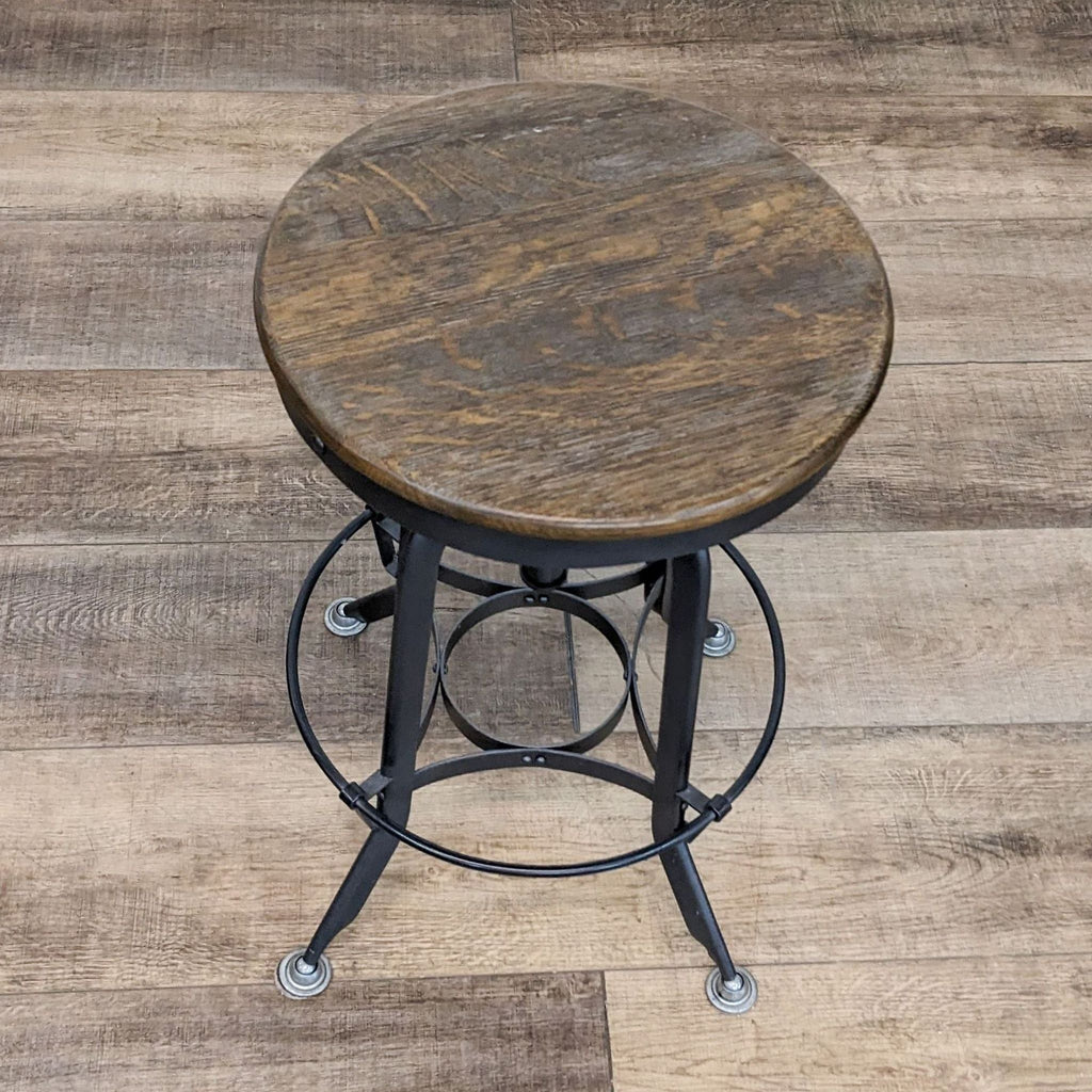Industrial style black metal stool with round rustic wooden seat, viewed from an angle.
