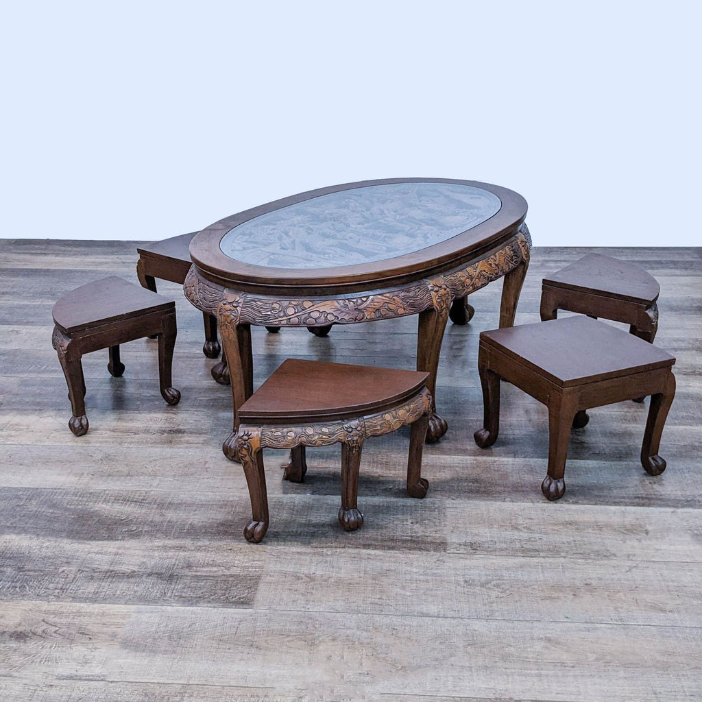 Oval wooden table with clear glass panel, detailed carvings, and six matching nesting stools.