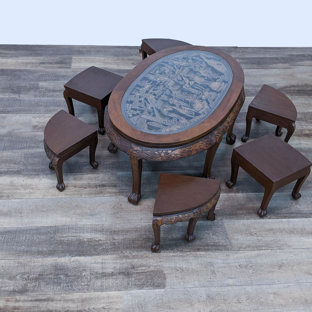 Solid wood oval table with carved figures, claw feet, and six nesting stools with shaped seats.