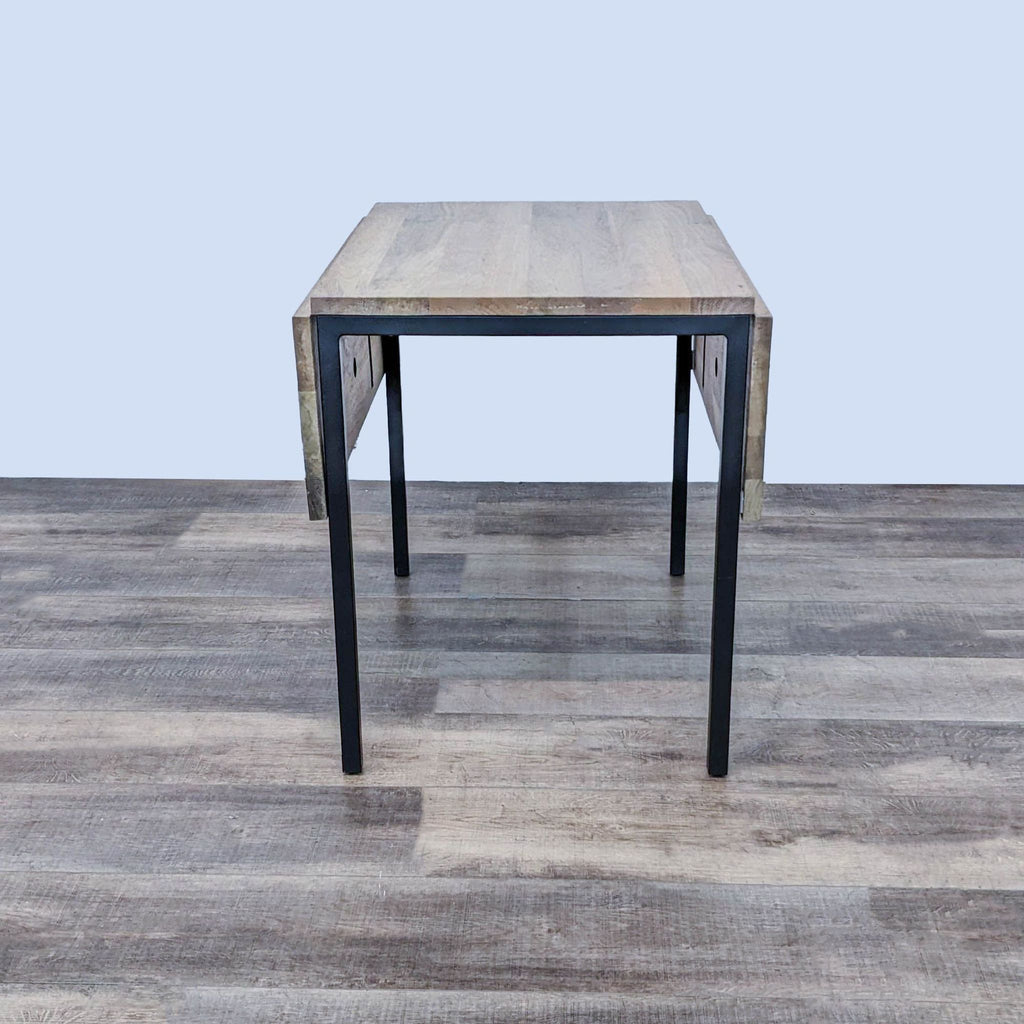 Compact West Elm Drop Leaf Table with one leaf up, set on a wooden floor.