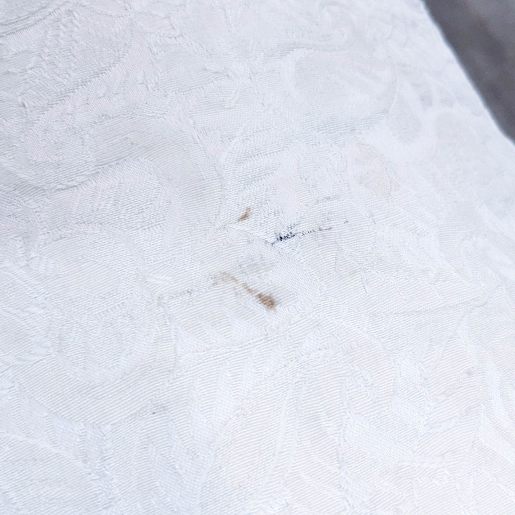 3. Close-up of a Drexel Heritage lounge chair fabric with small stains, highlighting the texture of the neutral embossed upholstery.