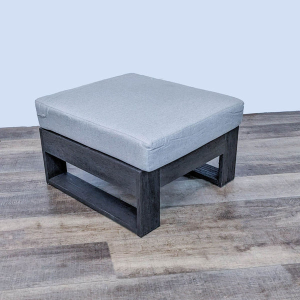 West Elm square ottoman with neutral Sunbrella cushion and dark wood frame on wooden floor.