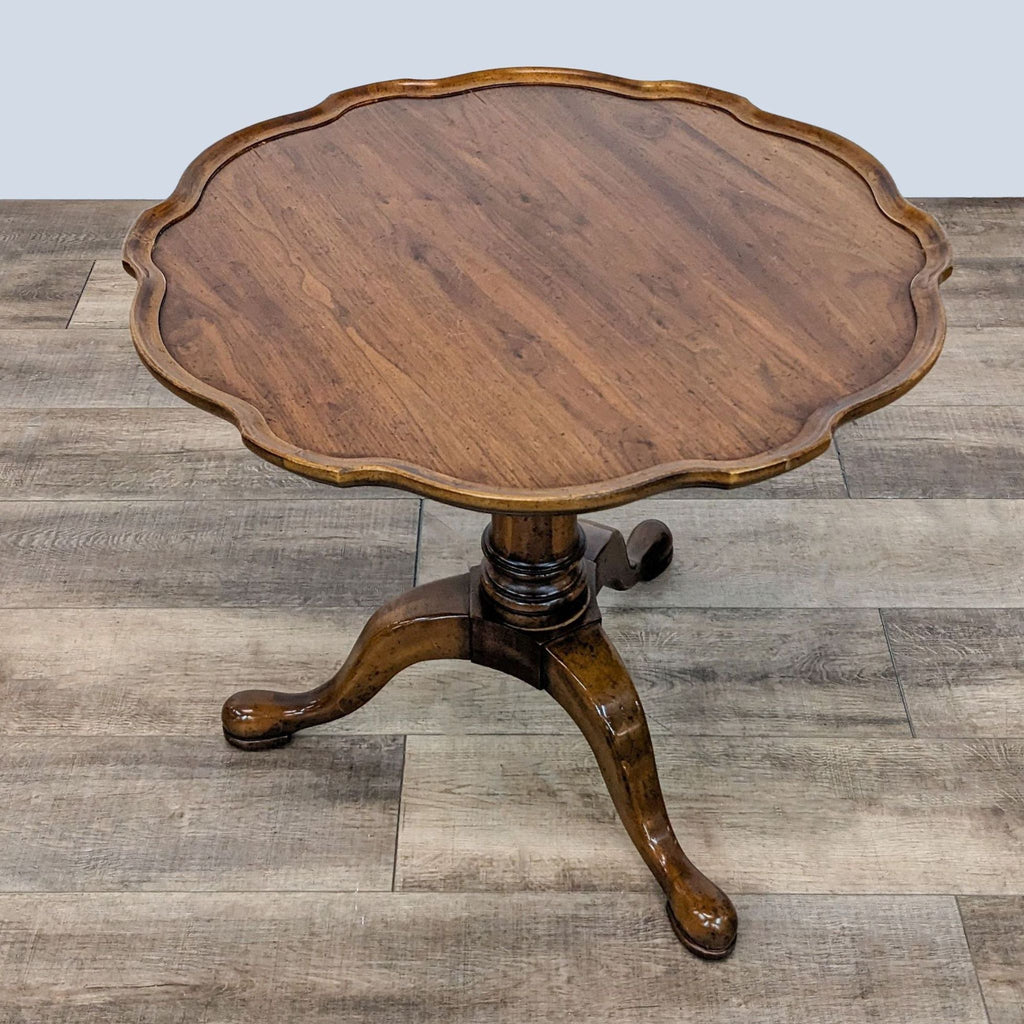 Elegant Reperch pedestal end table with a round, contoured top and curved legs, showcased on a wooden floor.