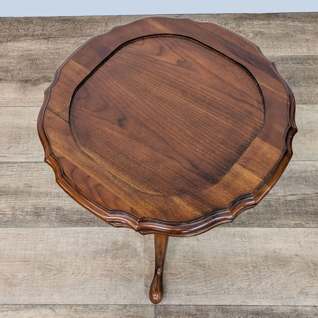 Top view of a round wooden Ethan Allen end table with scalloped edges on a wooden floor.