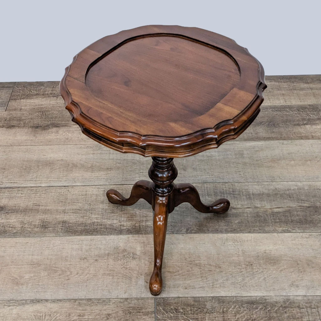 Angled view of an Ethan Allen round end table with scalloped edges, pedestal base, on a wood-textured floor.