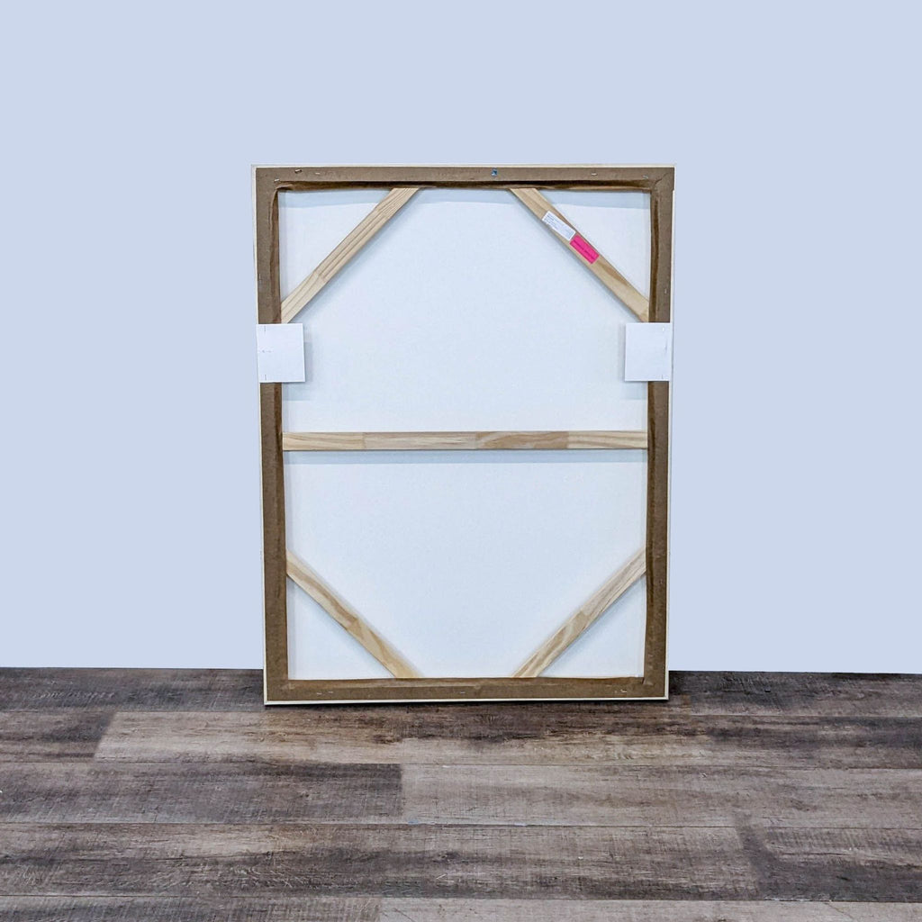 2. Rear view of a framed giclee painting showing the wooden floater frame construction and hanging hardware against a wooden floor backdrop.