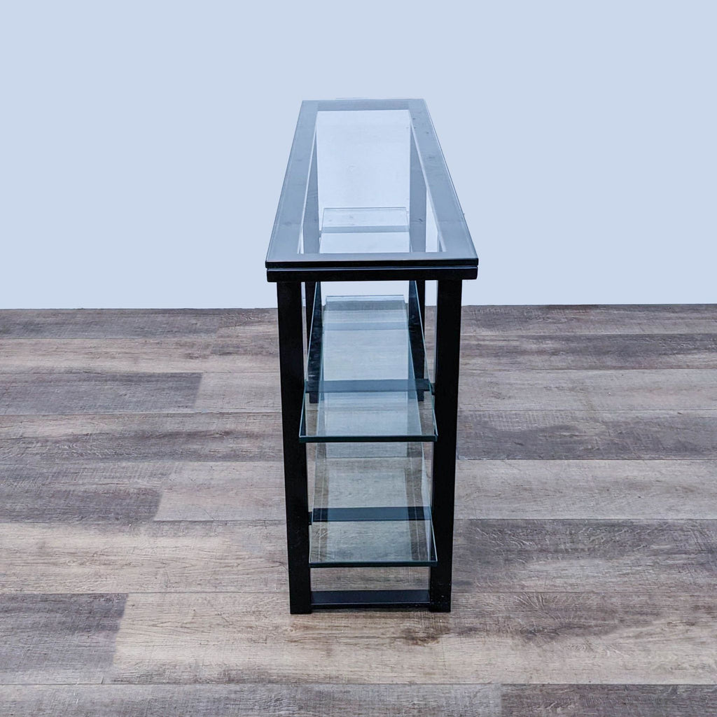 Front view of a Crate & Barrel side table with three glass shelves, metal frame, on a wooden floor.