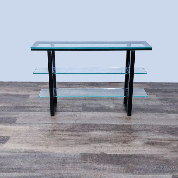 Crate & Barrel metal frame console table with a glass top and two lower shelves, against a wood floor background.