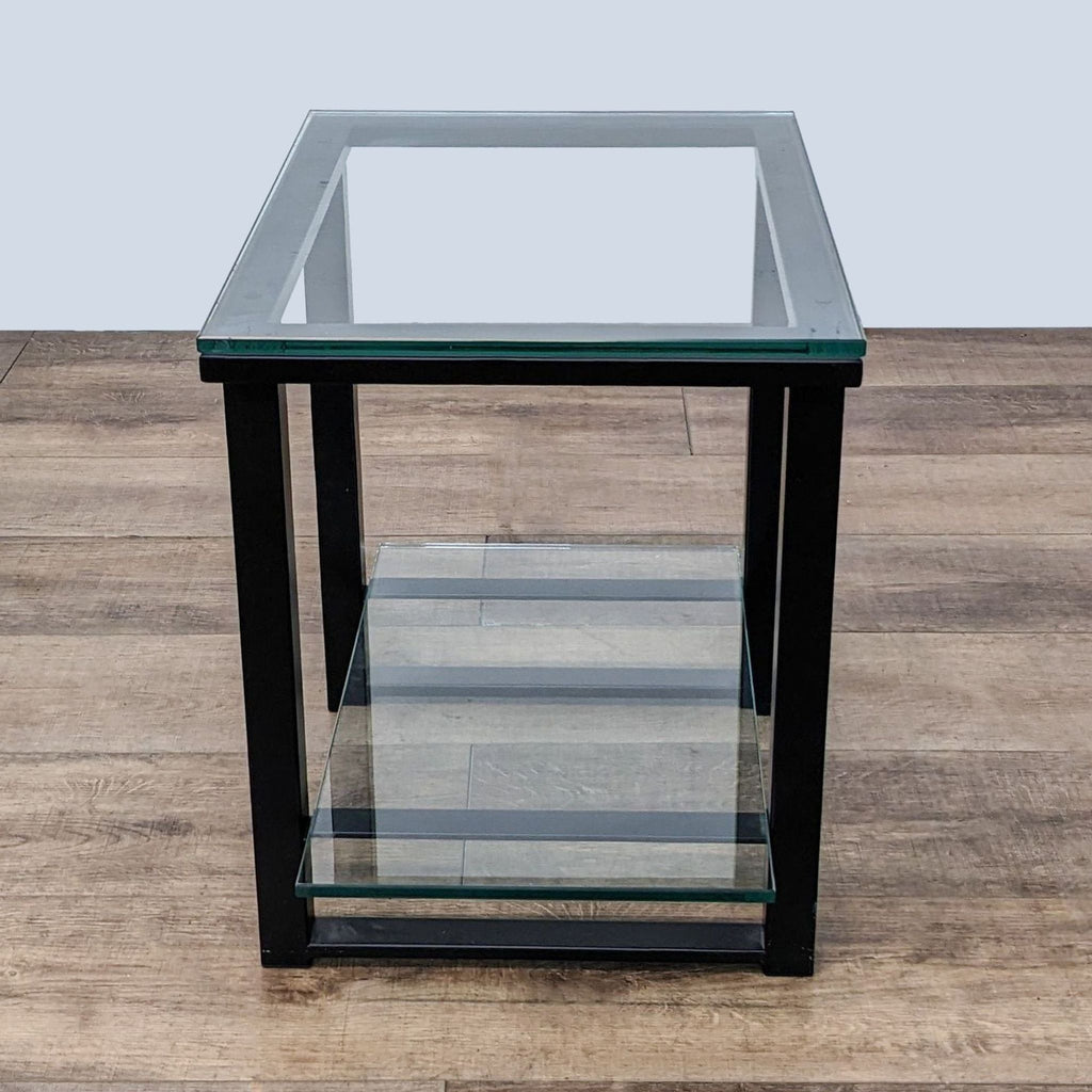 Metal-framed end table by Crate & Barrel with clear glass top and shelf, wooden floor background.