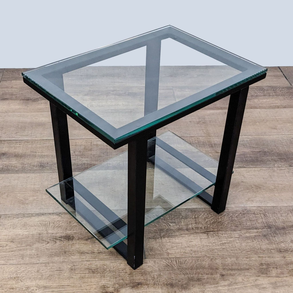 Modern Crate & Barrel glass-topped end table with metal supports and a lower glass shelf, angle view.