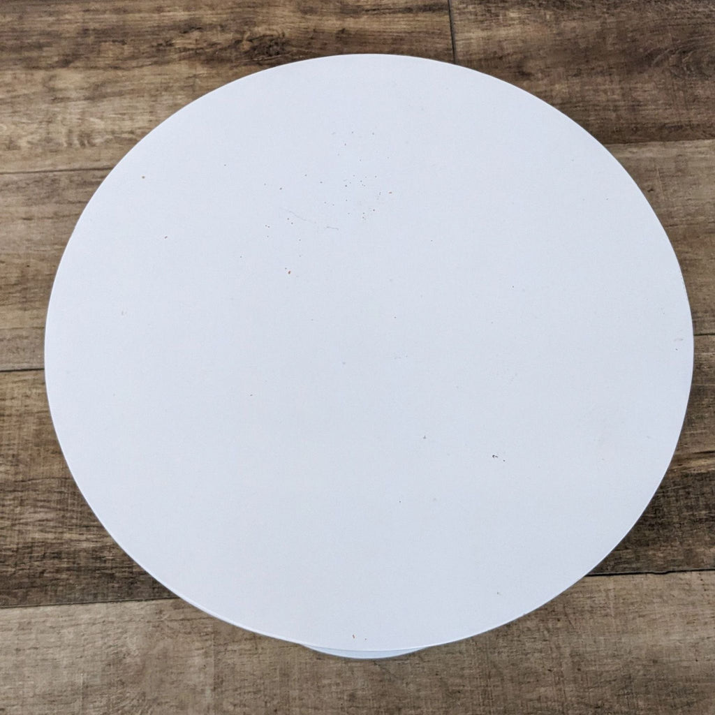 3. Top-down view of a circular West Elm aluminum end table's flat, white tabletop surface with wooden floor background.