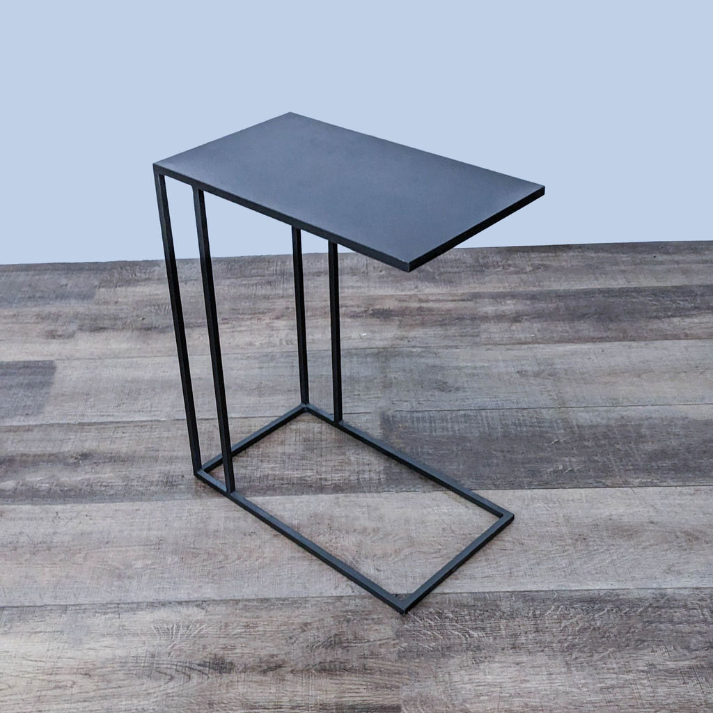 Angular West Elm side table with a cantilevered top design and metal frame on a plank-style floor.