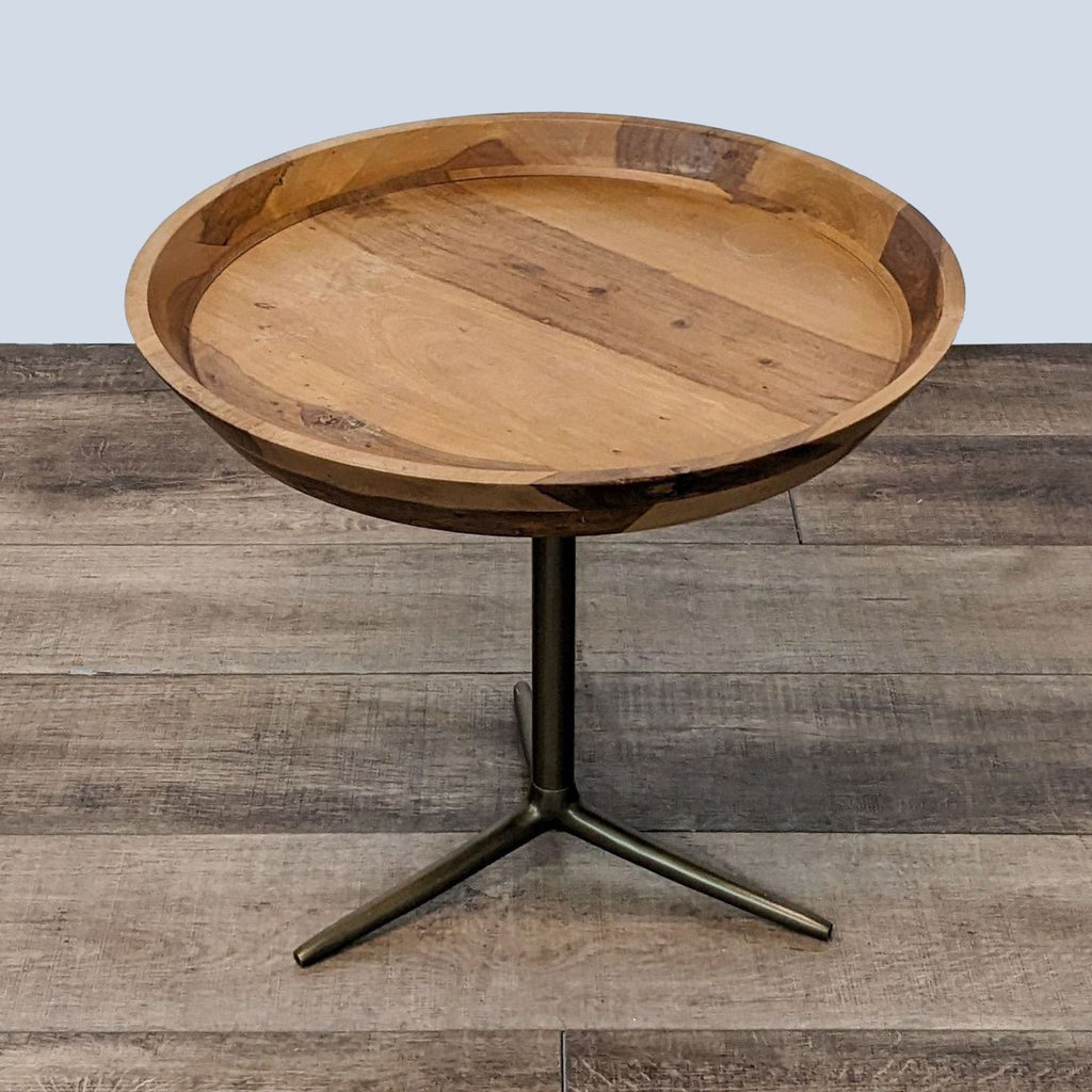 Round wooden tray top end table by West Elm, on a tripod metal base, set against a wooden floor.