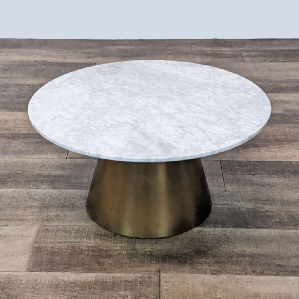2. Round marble-topped coffee table by Article with a sturdy golden base, displayed on a wooden floor.