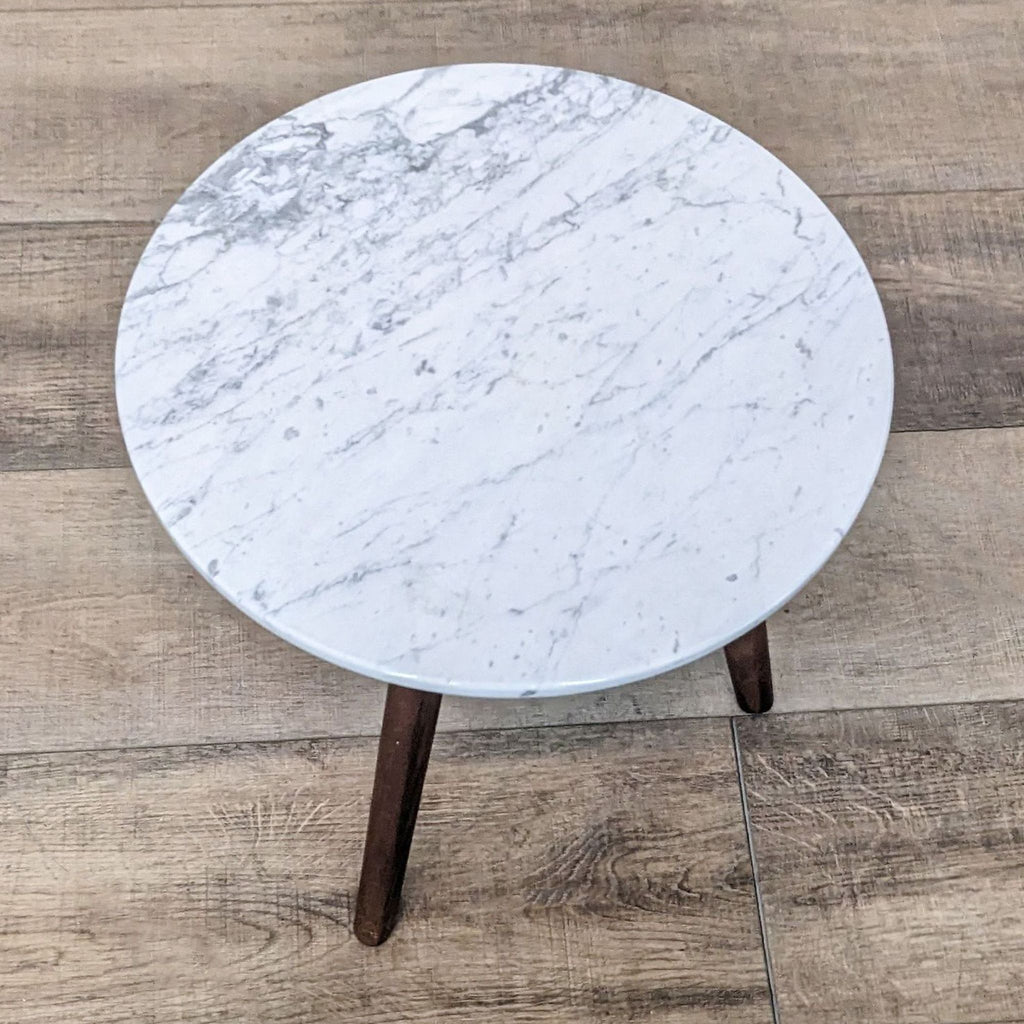 Stylish side table with a marble top and dark wooden legs on a wooden floor.
