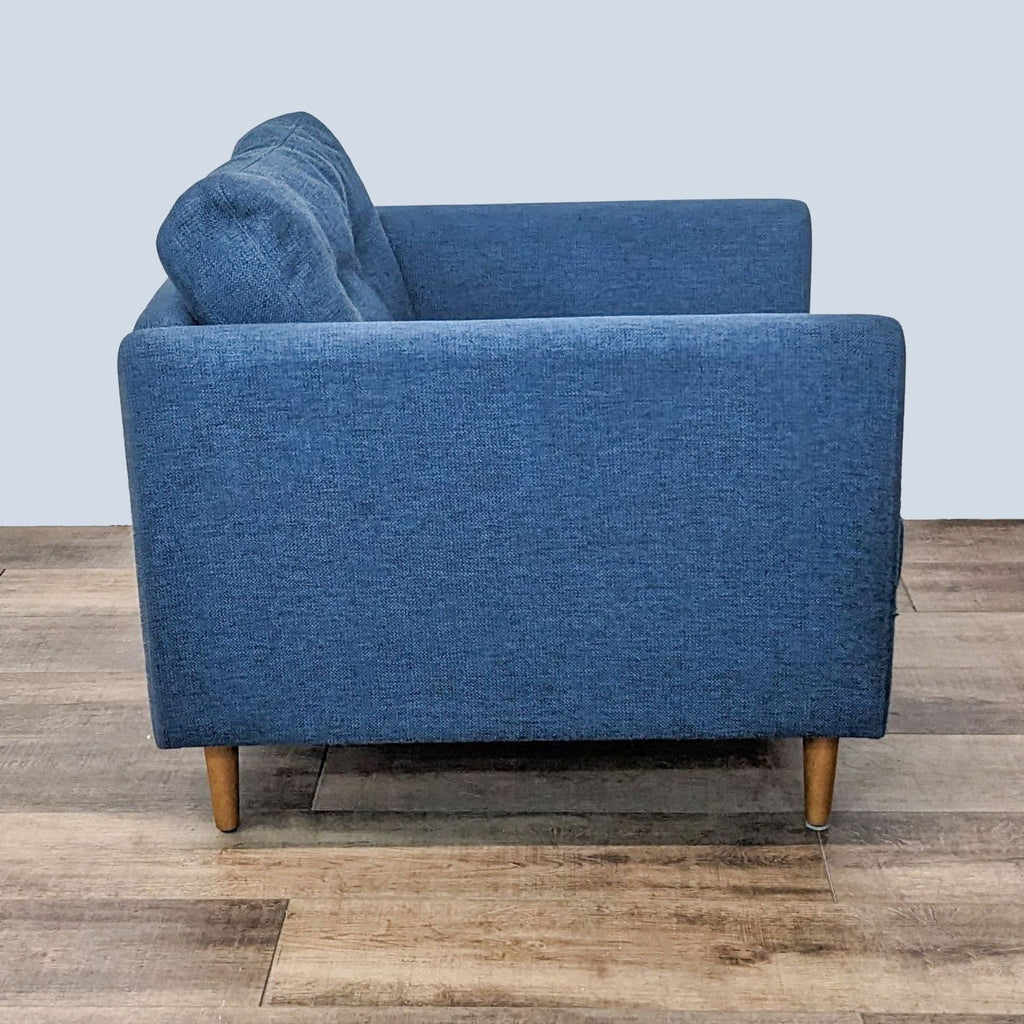 2. "Rear view of a stylish denim blue lounge chair by Article, showing solid wooden legs and the back's fabric texture, on a wooden floor."
