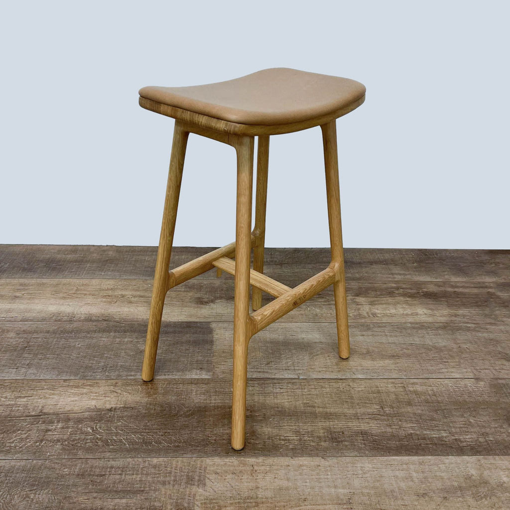 Article brand stool with soft leather upholstery and sturdy oak legs, angled view.