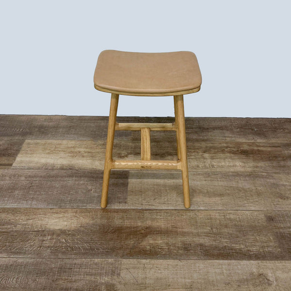 Oak wood counter stool with a cushioned tan leather seat by Article on wood floor.