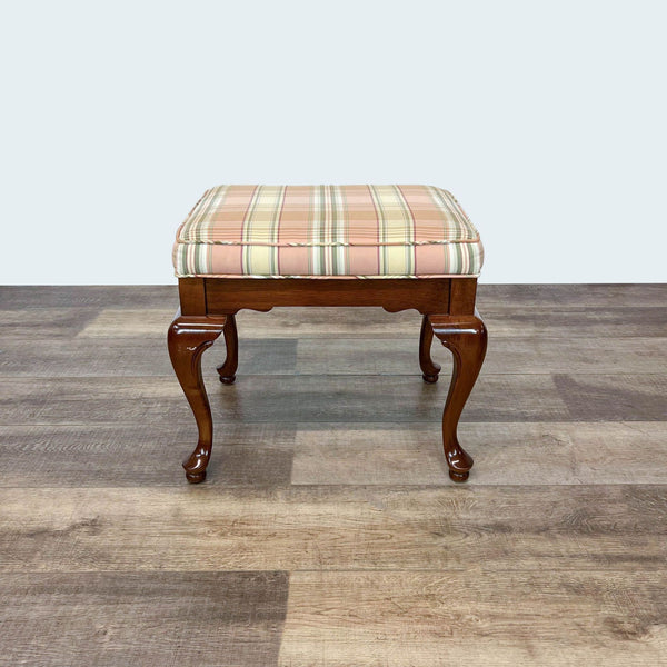 Queen Anne style wooden bench by Reperch with plaid padded seat on laminate floor.