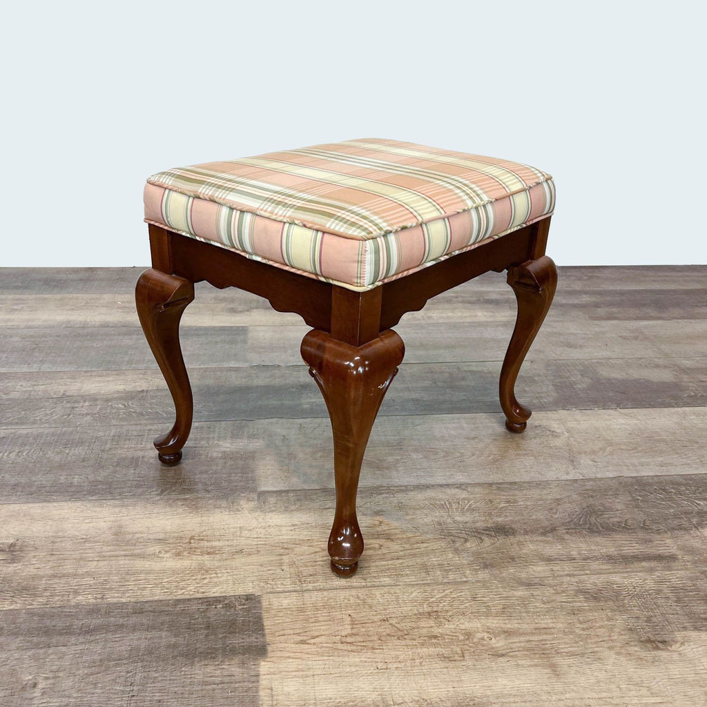 Elegant Reperch stool with plaid cushion and curved legs, in a Queen Anne style, on hardwood.