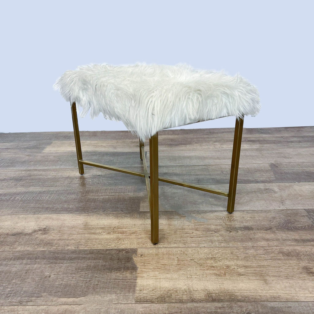 3. Side perspective of a fluffy off-white bench with a metallic gold base from Reperch, placed on a wooden floor.