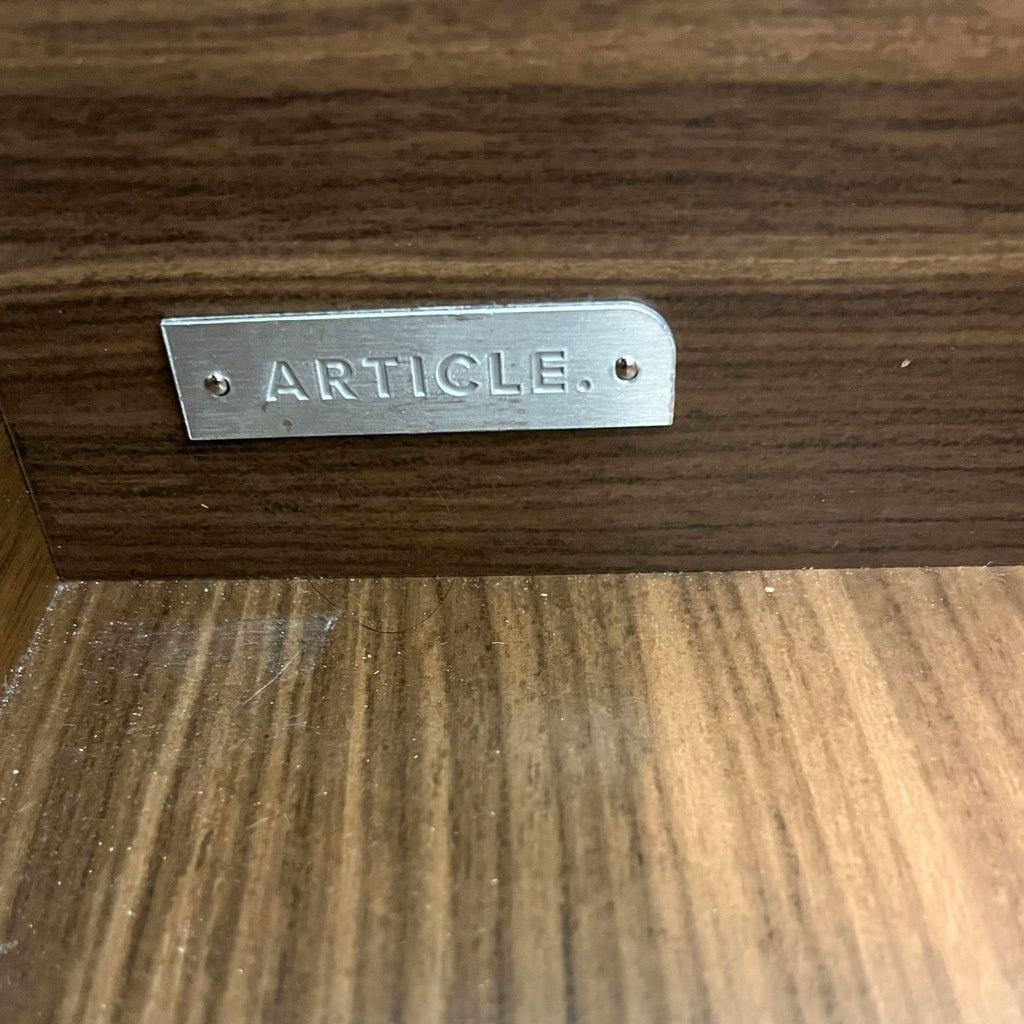 3. "Detail of a metal brand badge marked 'ARTICLE.' on the front of a wooden Nera dresser drawer."