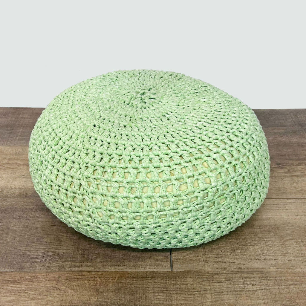 Round green pouf with weave pattern, resting on wood surface.  