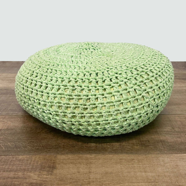 Green Reperch woven pouf ottoman on wooden floor against white backdrop.