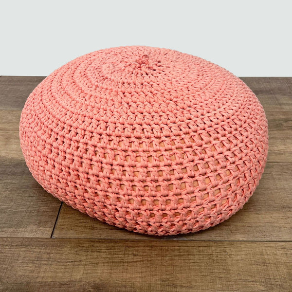 1. Round coral knitted pouf ottoman by Reperch with visible stitching on a wooden floor.