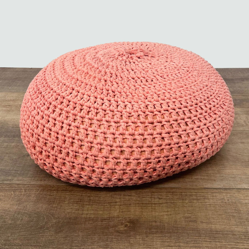 3. Reperch’s coral-colored knitted pouf ottoman with a textured surface, placed on a hardwood floor.