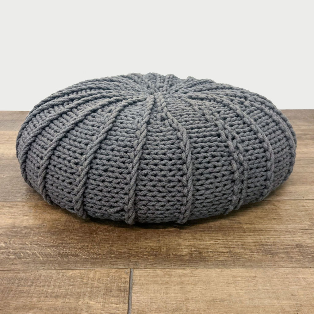 2. Grey hand-knit style pouf by Reperch seen from an angle, showcasing its unique design on a wooden floor.