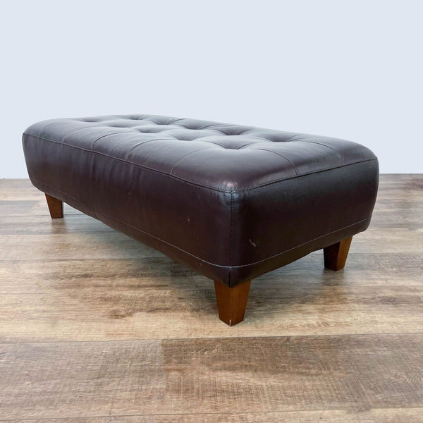 1. Chateau d'Ax brown leather tufted ottoman bench with wood finish feet on hardwood floor.
