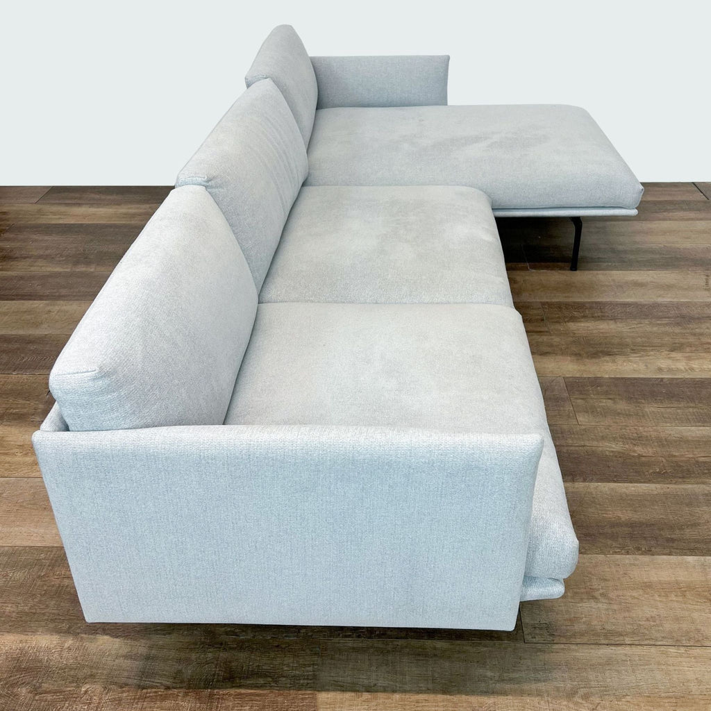 Corner view of a textured light gray sectional sofa on a wooden floor, showcasing depth and design.