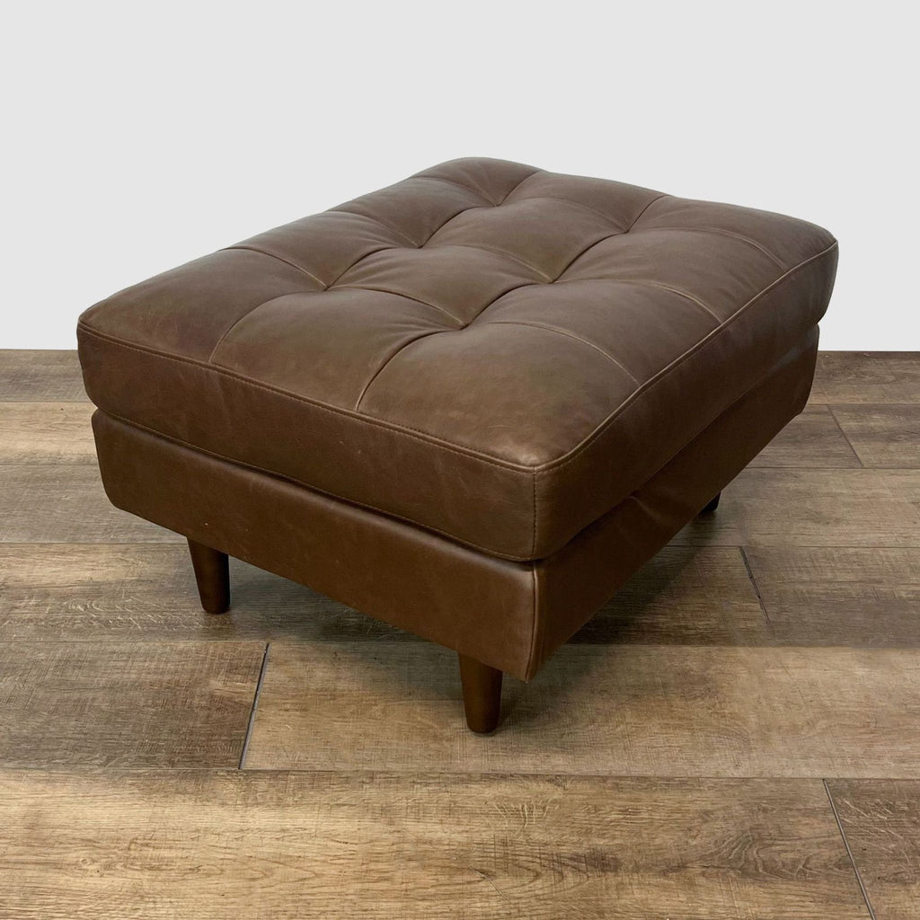 2. Article brand brown tufted leather ottoman on wooden floor, showcasing mid-century design and tapered legs.