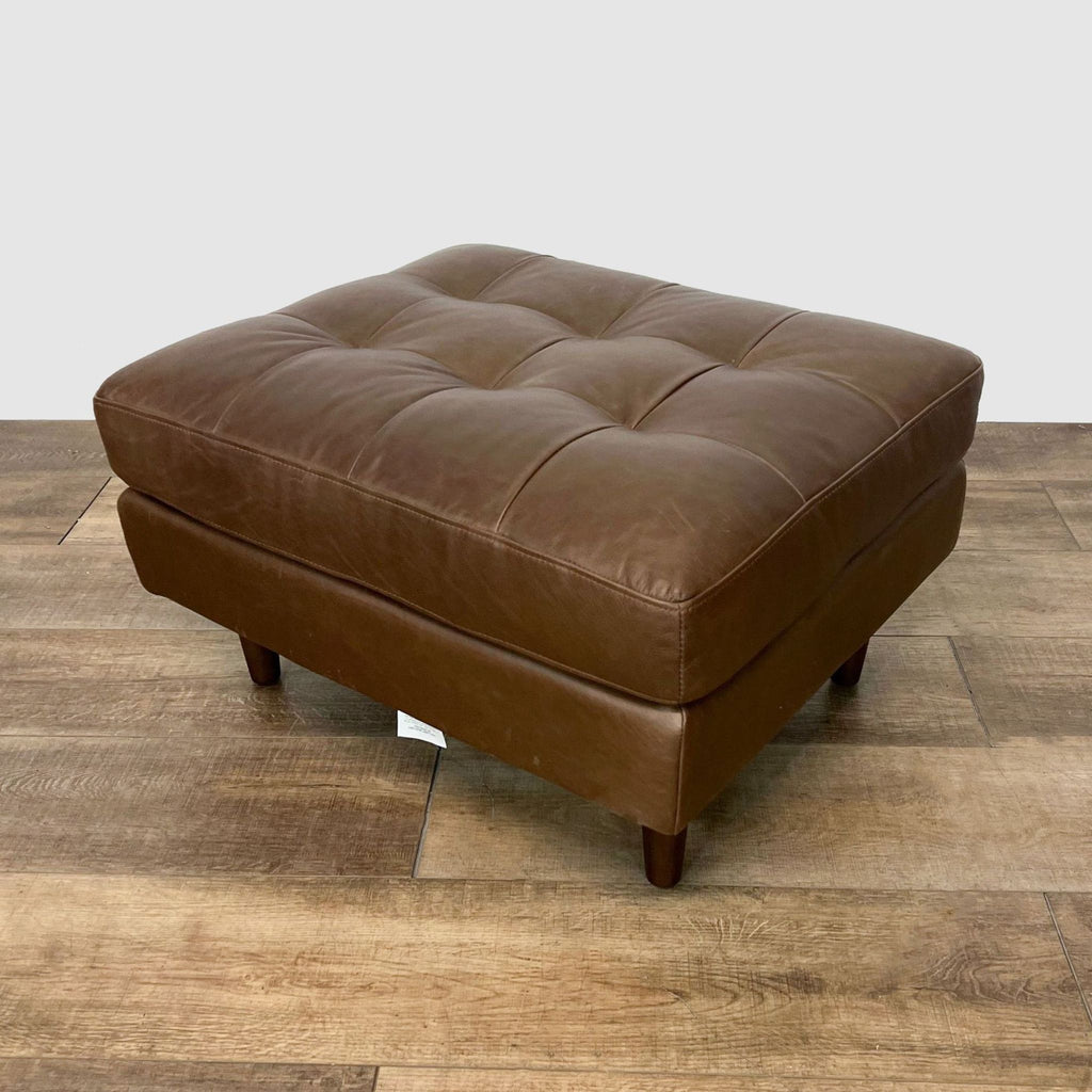 3. Mid-century style Article ottoman with tufted brown leather and wood feet, displayed on herringbone-patterned flooring.