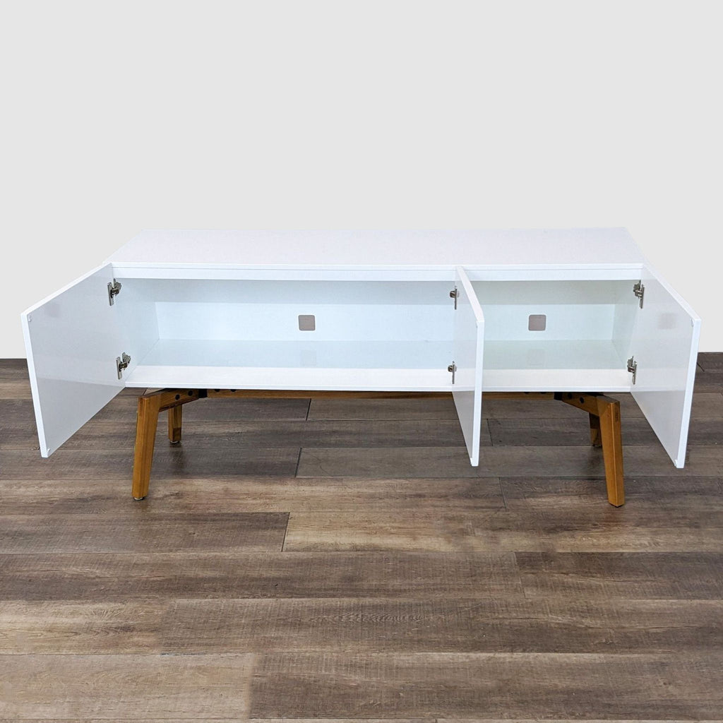 2. Open CB2 white credenza showing large storage space with cable management cutouts, supported by angled walnut legs.