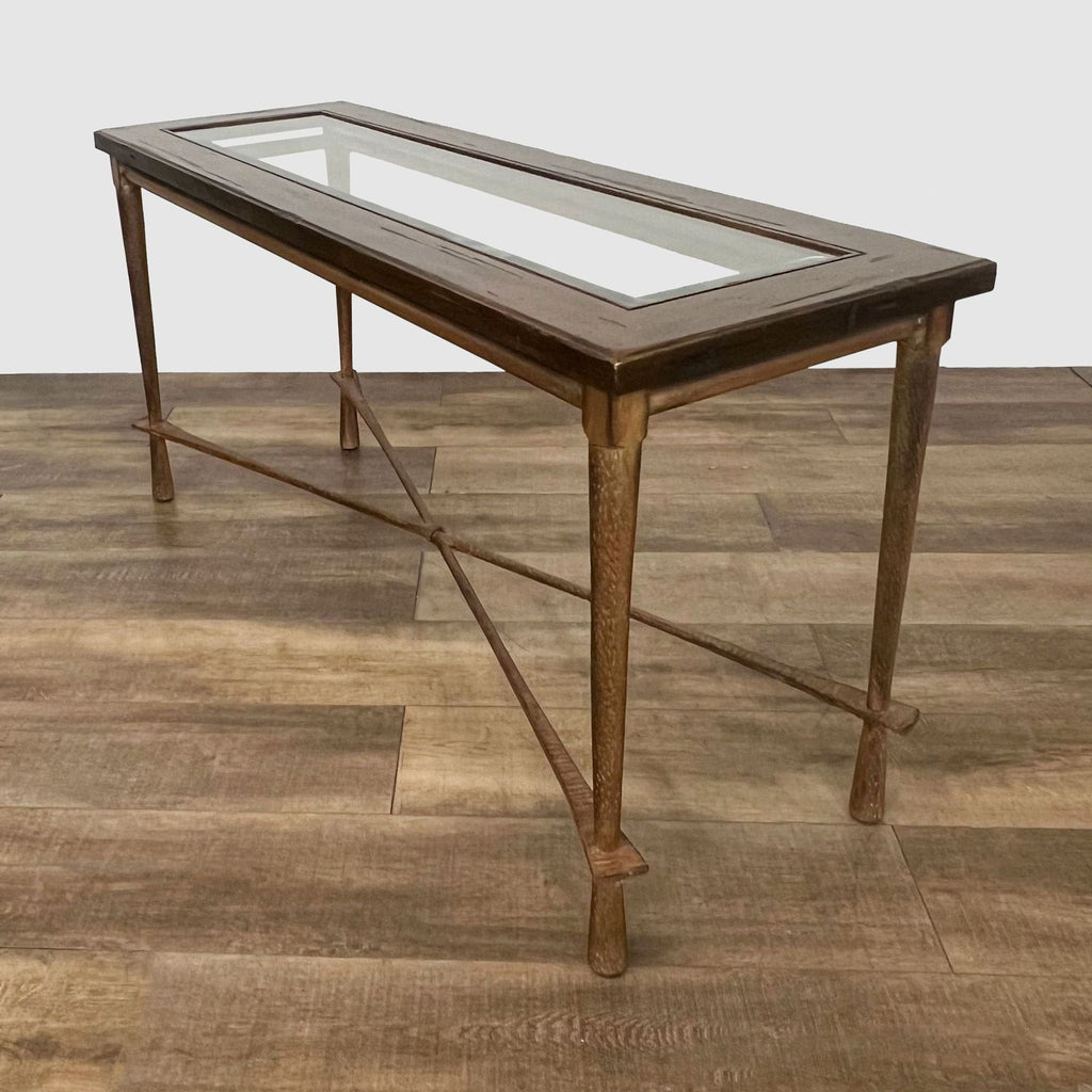 Elegant Reperch table with glass panel, wooden frame supported by intersecting metal stretchers on a textured floor.