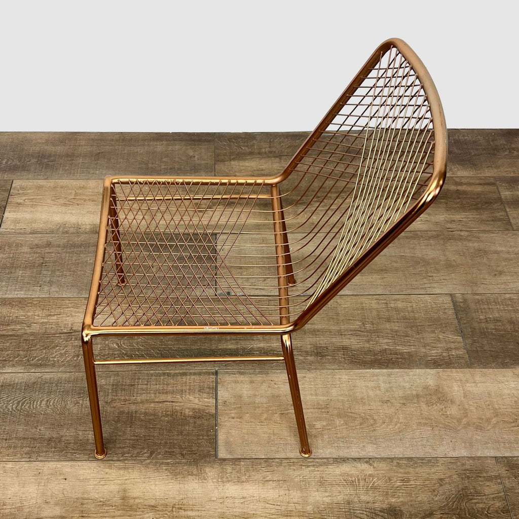 Angled view of a CB2 Modern Beta metallic chair showcasing its intricate wire backrest and linear pattern against a wooden floor.