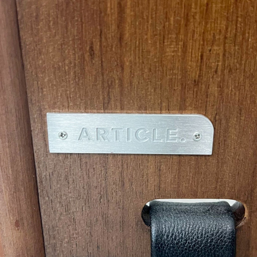 Branding detail of Article on the Beau mirror's walnut frame with leather strap accent.