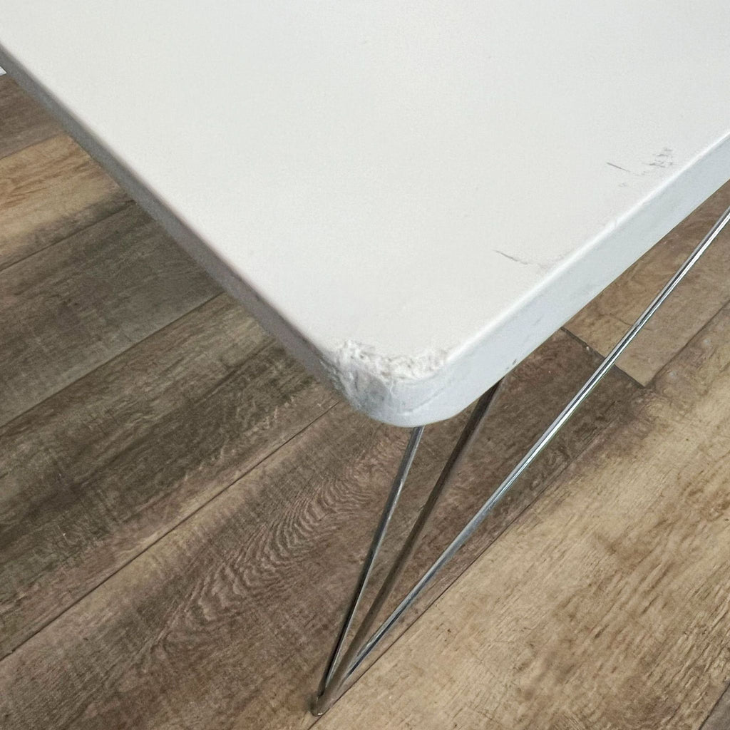 Close-up of a Reperch table corner showing wear, with its steel legs on wooden floor.
