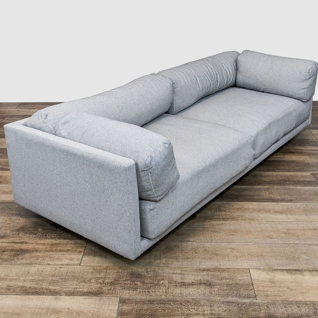 2. Angled view of a Blu Dot Sunday 3-seater sofa showing the extra deep cushioning and recessed wooden legs, set on a wood floor.