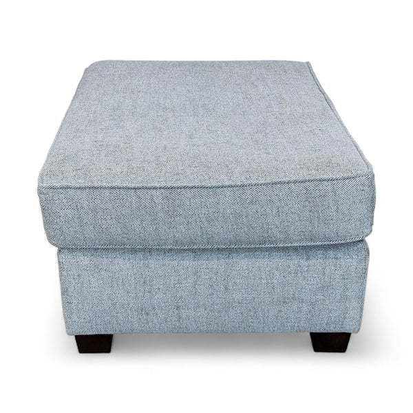 Gray Reperch upholstered ottoman with a smooth top and dark wooden legs, isolated on white.