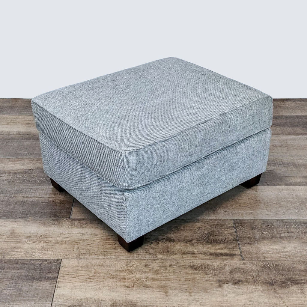 Reperch gray fabric ottoman on a wooden floor, versatile for footrest or seating.