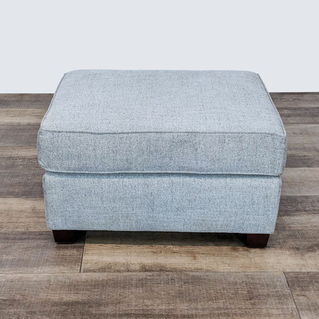 Close-up view of a Reperch gray upholstered rectangular ottoman with wooden legs in a room.