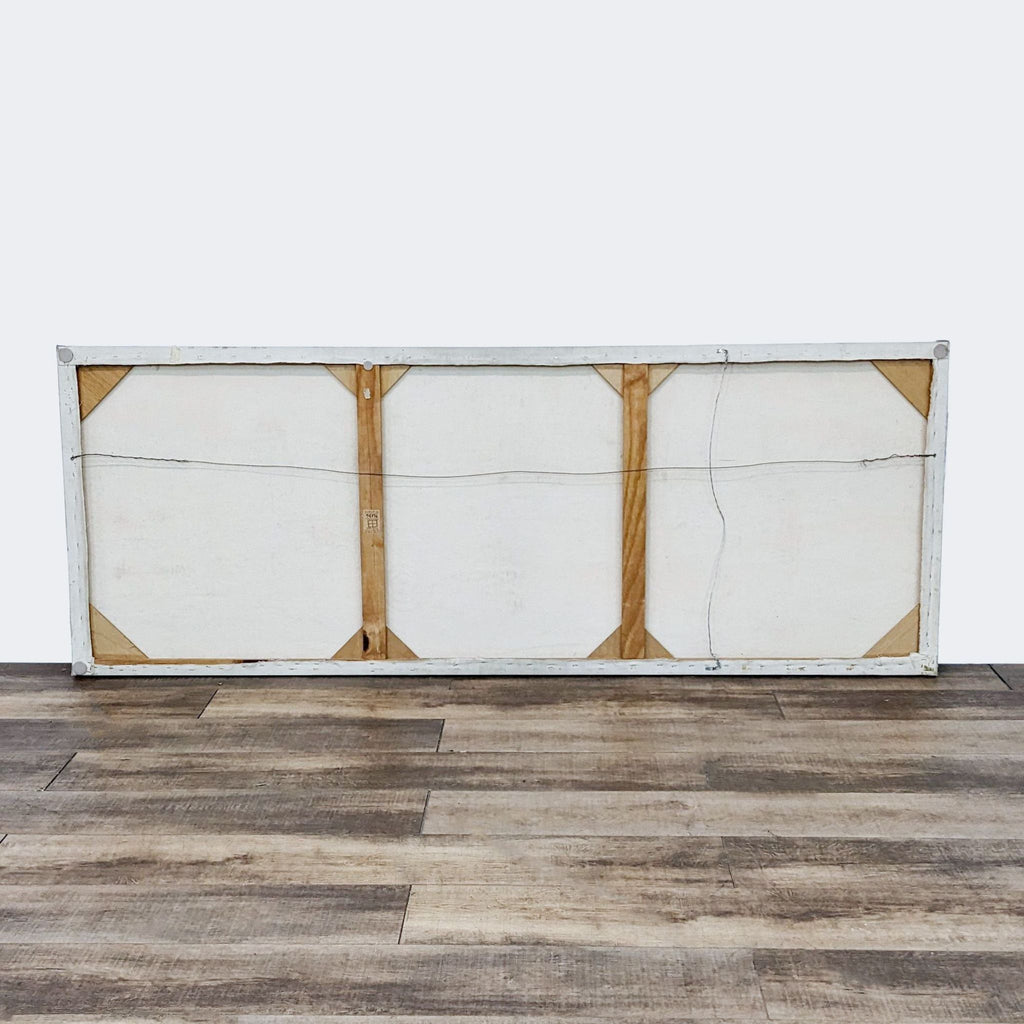 Rear view of a stretched canvas showing the wooden stretcher frame against a wood floor backdrop.