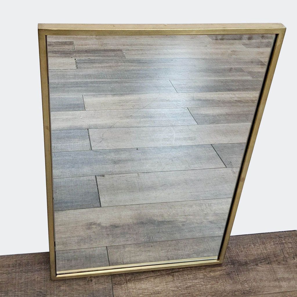 West Elm minimalist style metal-framed rectangle mirror leaning against a wooden wall.